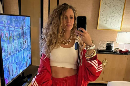 Blake Lively takes a mirror selfie in a stylish room. She wears a red tracksuit, white crop top, and chunky jewelry.